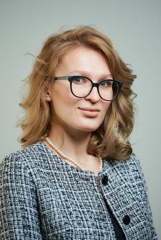 A stylish young woman in glasses dressed in a grey skirt suit with a black shirt. A close-up portrait of a blond lady who wears a business outfit. A concept of an office style wardrobe.
