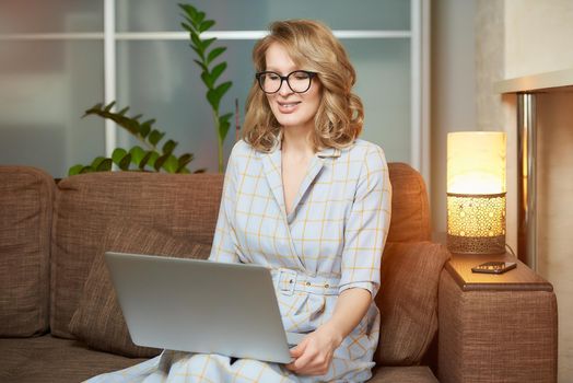 A young woman in glasses works remotely on a laptop in her apartment. A lady during a video business briefing at home. A pretty female student with braces listening to an online lecture.