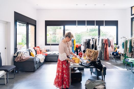 business woman, fashion shop owner, placing handbags on a display stand in her shop. shopping concept. natural light from the shop window, sun rays, display with clothes, clothes rack, shop window, clothes, vertical.