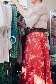 cropped shot of a woman picking up and buying clothes in a fashion shop. concept of shopping.concept of leisure. natural light from the shop window, sun rays, display with clothes, clothes rack, shop window, clothes, vertical