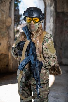 Portrait of a woman in a helmet and goggles with a machine gun in her hands. A female soldier in a camouflage uniform holds a weapon