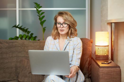 A young woman in glasses works remotely on a laptop in her apartment. A lady during a video business briefing at home. A pretty female student listening to an online lecture.