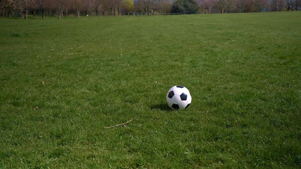 Panorama Wide Shot Black White Classic Soccer Ball On Green Grass. Happy Family Of Children Having Fun In Spring Park. People Playing Football. Sport, Healthy Life, Championship, Competitions Concept.
