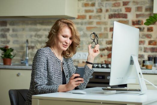 A woman with glasses works remotely on a desktop computer in her studio. A boss distracted by smartphone during a video conference at home. A happy professor uses a cellphone before an online lecture..