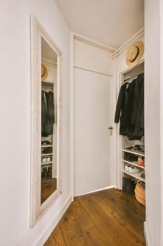 White wardrobe located against mirror and door leads to another room in light narrow corridor