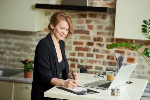 A young woman works remotely on a laptop in her kitchen. A female boss is happy with her employees during a video conference at home. A teacher writing answers of students during an online lecture..