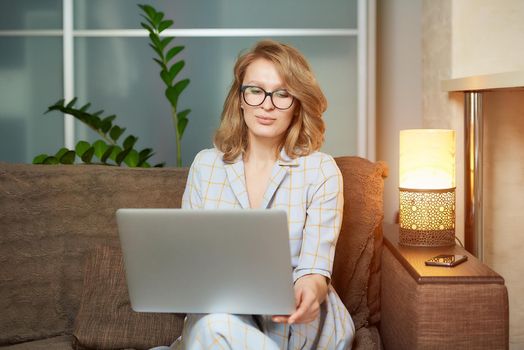 A young woman in glasses works remotely on a laptop in her apartment. A lady during a video business briefing at home. A pretty female student listening to an online lecture.