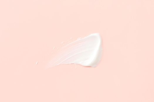 Delicate white moisturizing smear of cosmetic lotion cream on pastel pink. Hygiene, creamy skin care product texture. Cosmetic cream for face and body, smeared spot pattern on color background