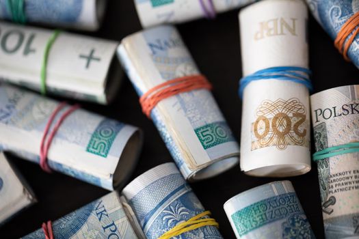 Several rolls of Polish banknotes in top view. Rolled up and fastened with a thin rubber band.