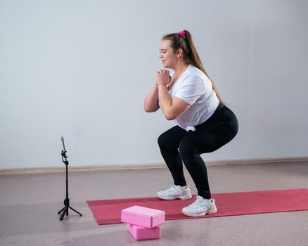 A chubby young woman is watching an online fitness lesson on a mobile phone. Distance sports training.