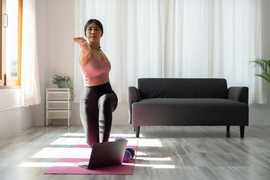 Young asian fitness trainer give yoga video lesson show stretching exercise before laptop webcam in conference mode. Motivated female take part in virtual sport training.