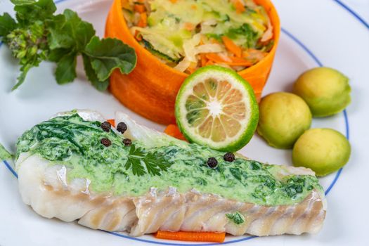 Cod back covered with sorrel sauce, accompanied by vegetables.