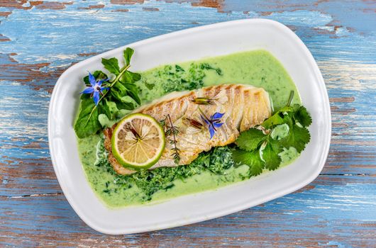 Close-up of grilled cod back on sorrel sauce, covered with coriander and lime.