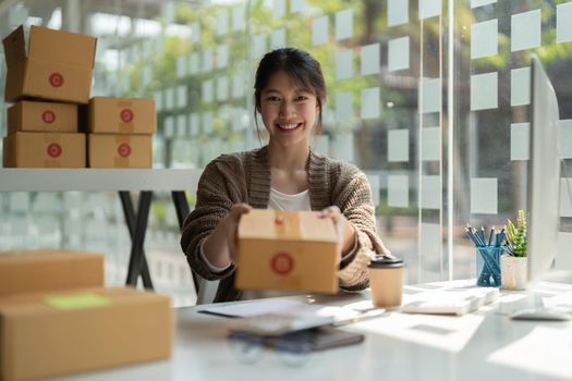 Young Asian Woman holding parcel box for delivery to customer by logistic service. small business entrepreneur SME distribution warehouse. small owner home office and Online marketing product theme.