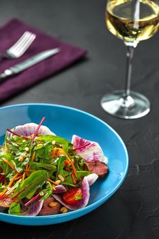 Spicy beef slices meat salad with tomatoes, parsley, radish and salad leaves spinach on black texture background table. Still life