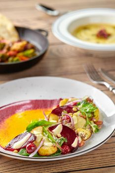 Healthy diet: colorful beetroot salad with potatoes and shredded leaves in a white plate on a wooden table