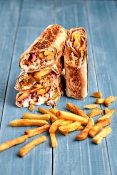 Middle Eastern Chicken Shawarma, Pita Sandwich, chicken roll in a pita with fresh vegetables, cream sauce and french fries on wooden background. Selective focus. Lunch snack. Still life