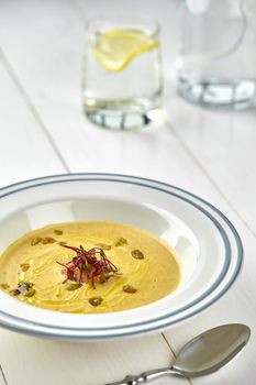 Healthy dinner with pumpkin soup-puree served in white bowl on white wooden table. Still life