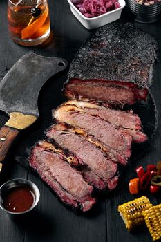 Fresh Brisket BBQ beef sliced for serving against a dark background with sauce, hot peppers and corn. Generous accommodation for copy space. American style