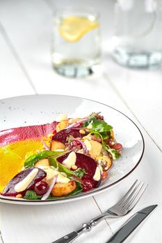 Healthy diet: colorful beetroot salad with potatoes and shredded leaves in a white plate on a white wooden table