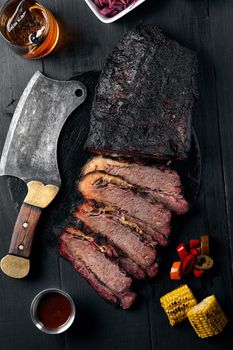 Fresh Brisket BBQ beef sliced for serving against a dark background with sauce, hot peppers and corn. Generous accommodation for copy space. American style