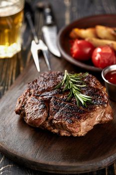 Juicy steak medium rare beef with spices on wooden board on table. dry aged. Served with potatoes, beer, and tomato sauce. Still life