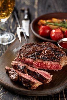 Juicy steak medium rare beef with spices on wooden board on table. dry aged. Served with potatoes, beer, and tomato sauce. Still life