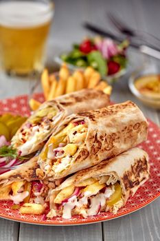 Middle Eastern Chicken Shawarma, Pita Sandwich, chicken roll in a pita with fresh vegetables, cream sauce and french fries on wooden background. Selective focus. Lunch snack. Still life