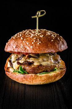 Cheese burger with grilled meat, cheese, tomato on dark wooden surface. Fast food template. Real photo. Ideal for advertisement. Close-up. Still life hamburger