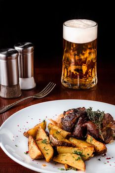 Pork knuckle with potatoes, cabbage and beer on a wooden table. Black background. Selective focus.