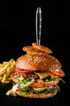 Cheese burger with grilled meat, cheese, tomato and with onion rings on dark wooden surface. Fast food template. Real photo. Ideal for advertisement. Close-up. Still life hamburger