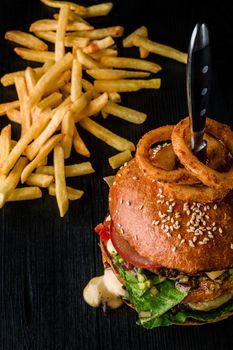 Cheese burger with grilled meat, cheese, tomato and with onion rings on dark wooden surface. Fast food template. Real photo. Ideal for advertisement. Close-up. Still life hamburger and French fries