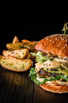 Cheese burger with grilled meat, cheese, tomato and potatoes on dark wooden surface. Fast food template. Real photo. Ideal for advertisement. Close-up. Still life hamburger