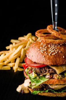 Cheese burger with grilled meat, cheese, tomato and with onion rings on dark wooden surface. Fast food template. Real photo. Ideal for advertisement. Close-up. Still life hamburger and French fries