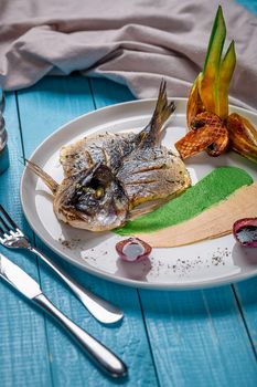 Fried fish dorado, decorated with cucumbers and onions. The original presentation of the dish from the chef. On a blue wooden background