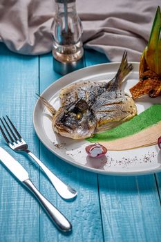 Fried fish dorado, decorated with cucumbers and onions. The original presentation of the dish from the chef. On a blue wooden background