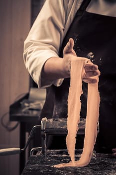 The chef makes fresh spaghetti from scratch. Wooden table. Photo in brown tones. Kitchen.