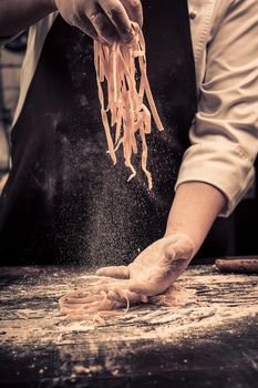 The chef makes fresh spaghetti from scratch. Wooden table. Photo in brown tones. Kitchen.