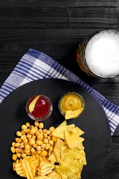 Overhead view of beer glass and snacks with sauce on black wooden table. Top view. Copy space. Still life. Flat lay