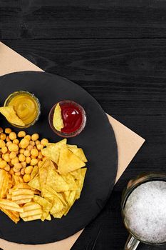 Overhead view of beer glass and snacks with sauce on black wooden table. Top view. Copy space. Still life. Flat lay