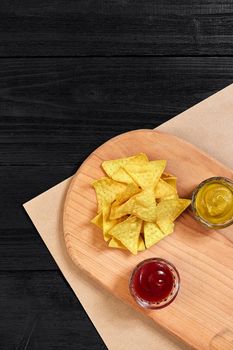 Tortilla chips with mustard and tomato sauce on black wooden table. Top view. Copy space. Still life. Flat lay