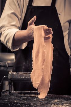 The chef makes fresh pasta from scratch. Wooden table. Photo in brown tones. Kitchen.