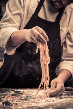 The chef makes fresh spaghetti from scratch. Wooden table. Photo in brown tones. Kitchen.