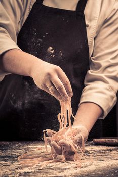 The chef makes fresh spaghetti from scratch. Wooden table. Photo in brown tones. Kitchen.