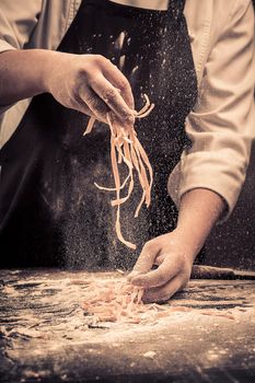 The chef makes fresh spaghetti from scratch. Wooden table. Photo in brown tones. Kitchen.