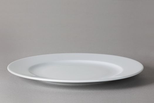 A flat front angle view of a white dinner plate on neutral background with shadow