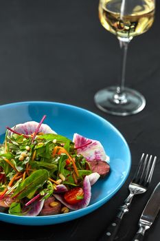 Spicy beef slices meat salad with tomatoes, parsley, radish and salad leaves spinach on black texture background table. Still life