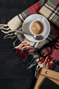 Above view of Smart phone with notebook and cup of latte coffee on black wooden background. Still life. Copy space. Flat lay. Top view