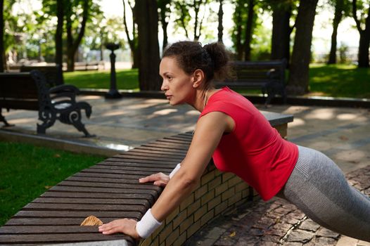 Middle-aged active African American woman doing pushups on the city park. Sport, fitness, outdoor workout, active lifestyle on sunny summer day, health and body care concept