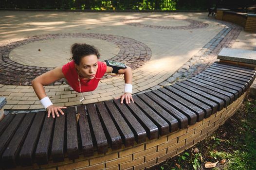 Determined active beautiful woman exercising outdoors,pushing ups from wooden bench while performing full body functional cross training outdoors. Sport, body weight training, weight loss concept